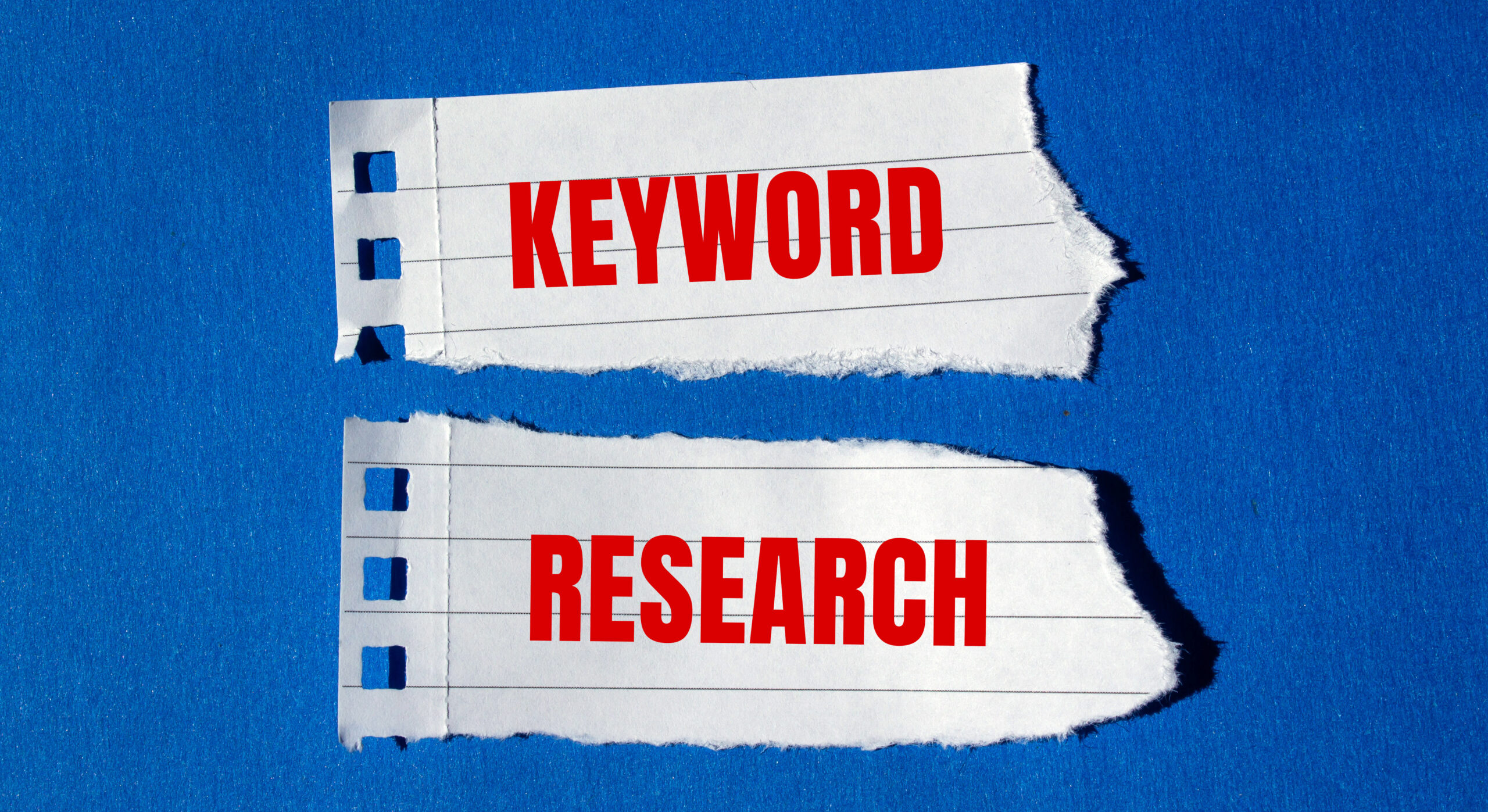 Keyword research message written on ripped torn paper pieces with blue background. Conceptual keyword research symbol. Copy space.